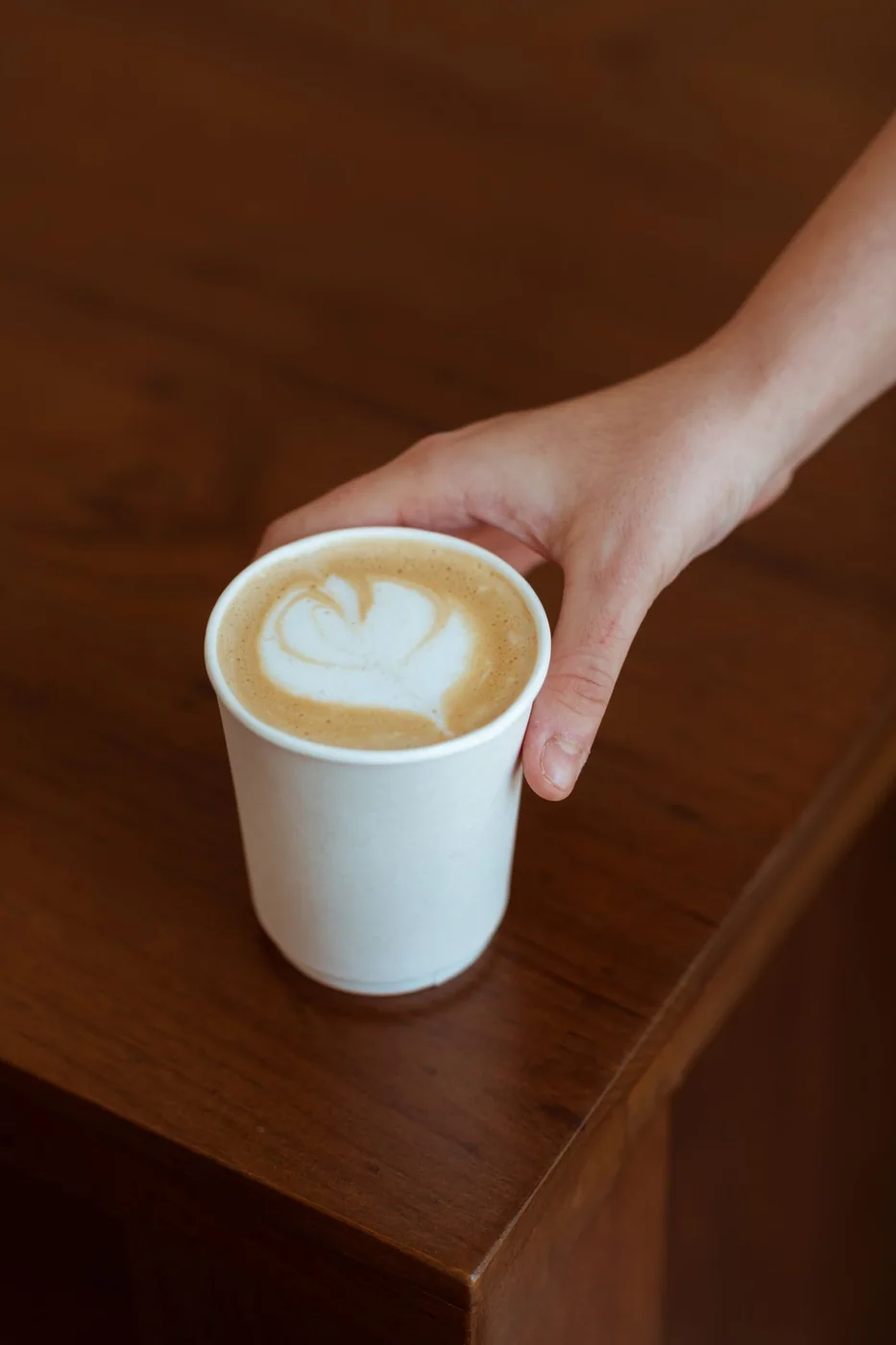Latte with leaf latte art in a white paper cup ready to serve
