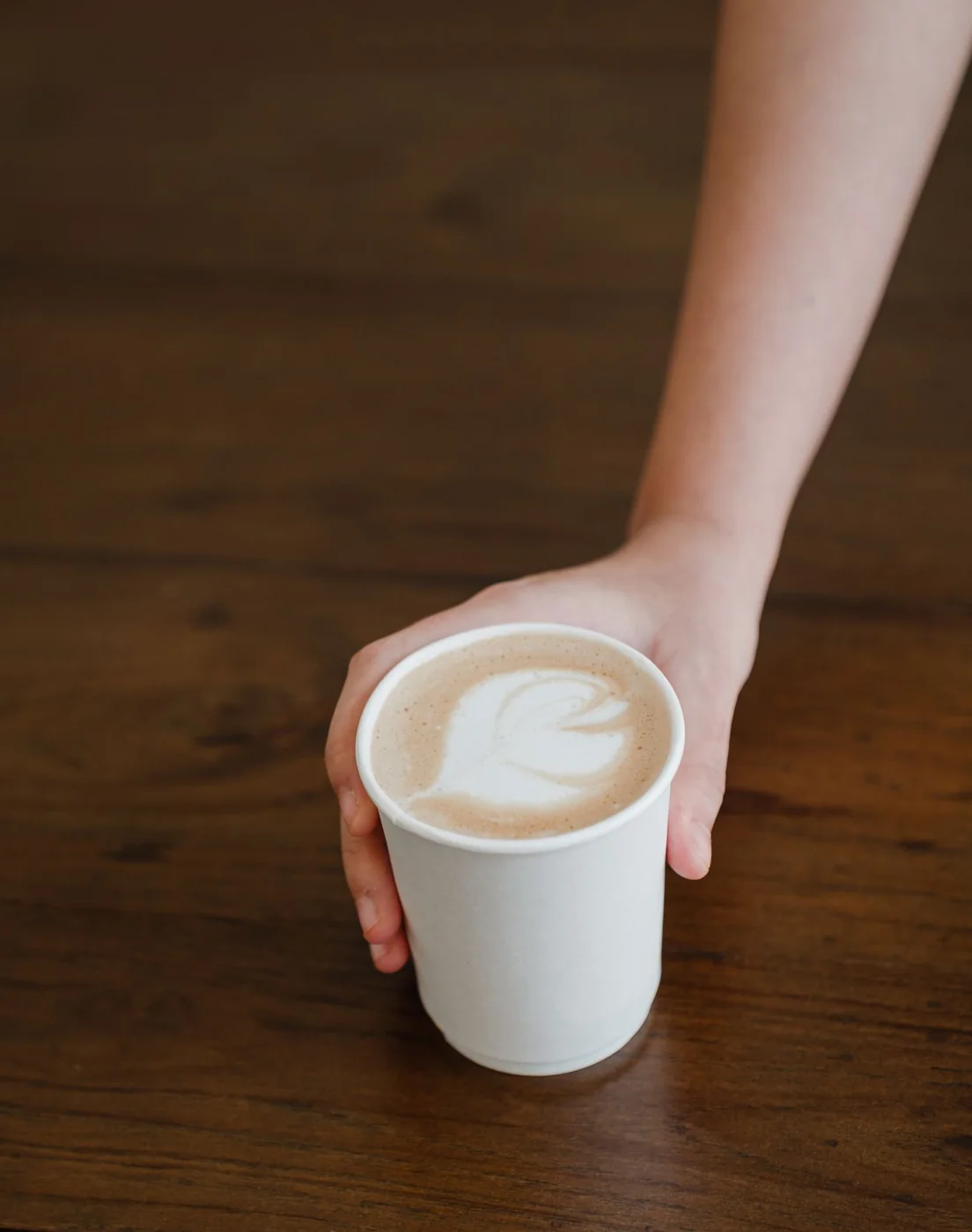 Barista serving a handcrafted latte in a paper cup at an event